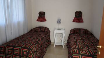 A room with two beds, a small white nightstand, and a lamp.