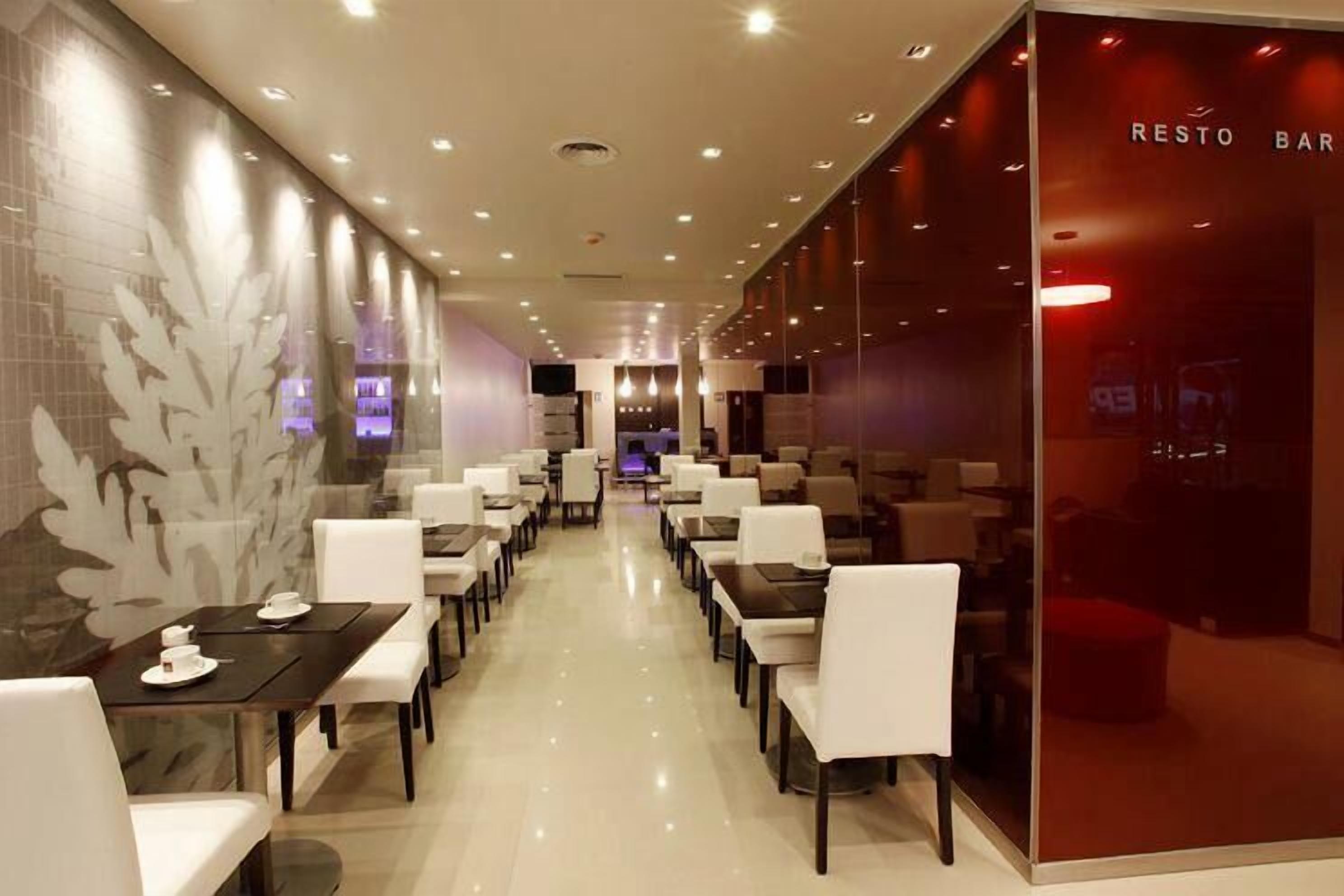 A modern restaurant with a long counter and white chairs, a glass wall with a red sign, and a patterned wall on one side.