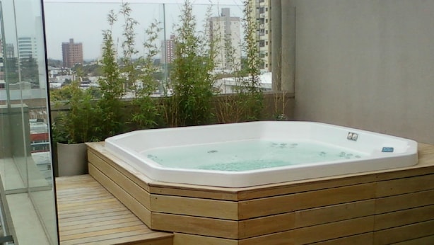 Una bañera de hidromasaje con escalones de madera que llevan a ella, frente a una vista panorámica de la ciudad.