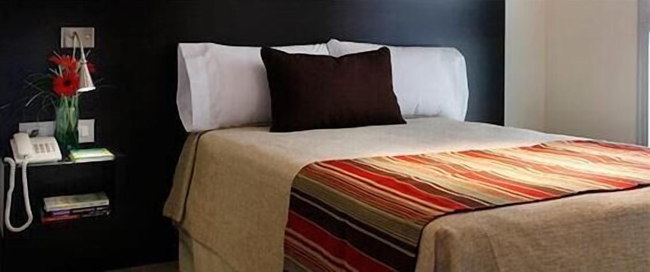 A neatly made bed with a striped blanket, a bedside telephone, and a vase with flowers on a nightstand.