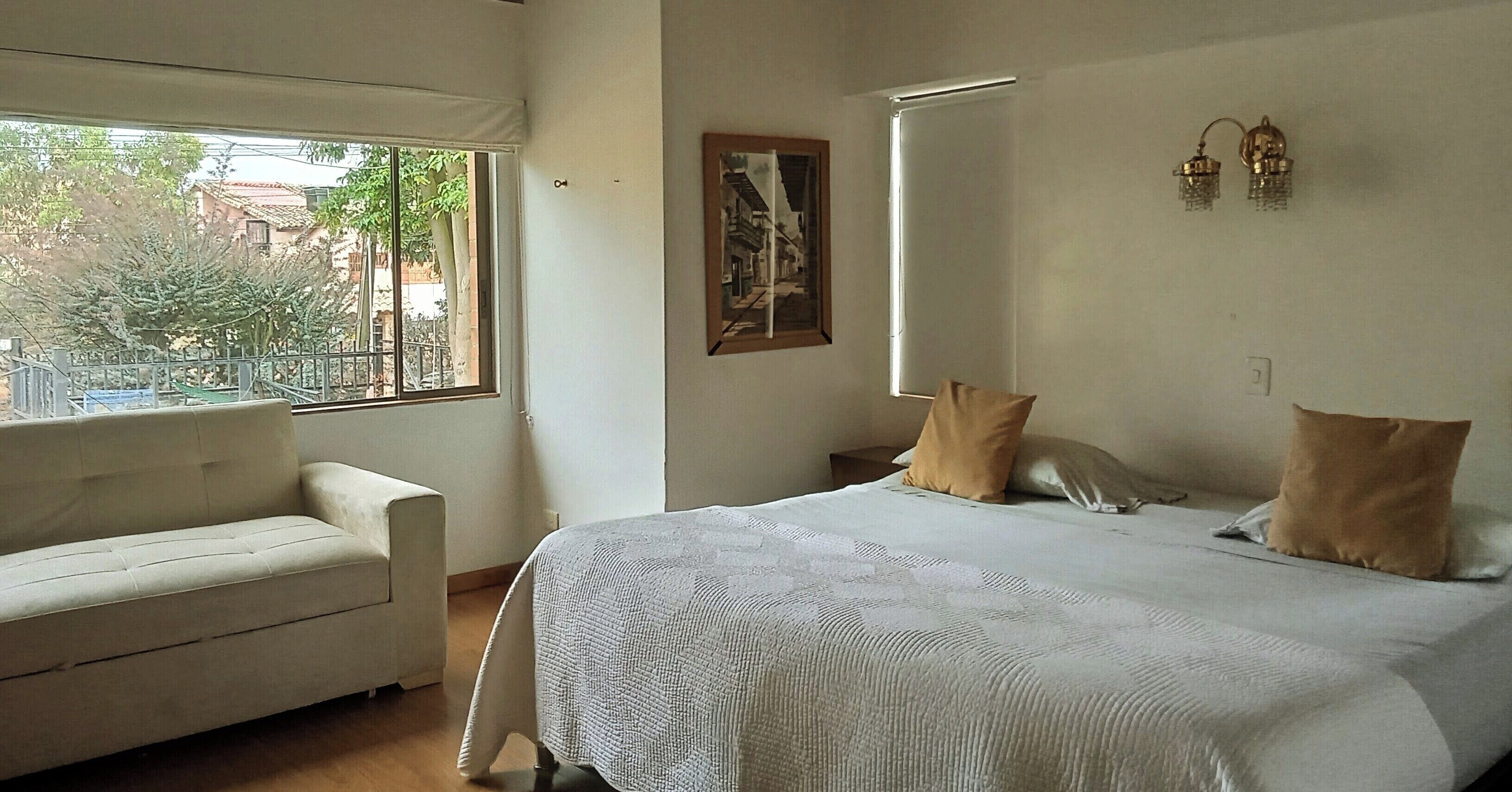 Un dormitorio con cama, sofá, ventana y un cuadro en la pared.