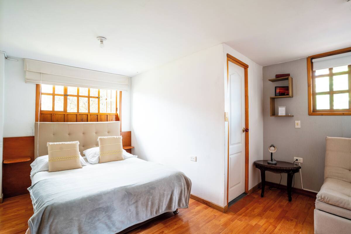 A bedroom with a bed, bedside table, lamp, chair, and a door leading to another room.