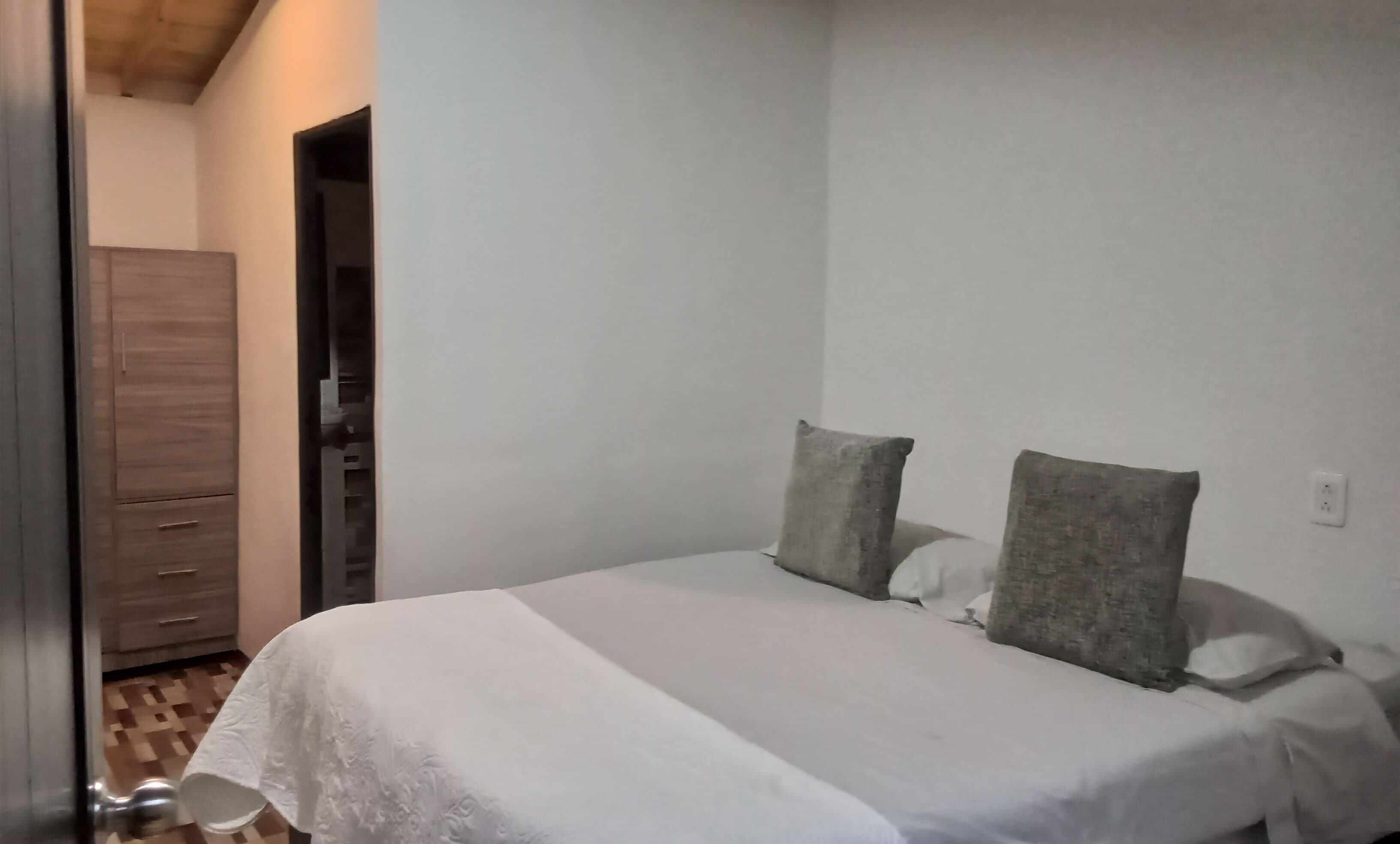 A bedroom with a bed, two pillows, a wardrobe, and a door.