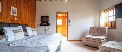 A bedroom with a bed, a chair, a television, and a wooden ceiling.