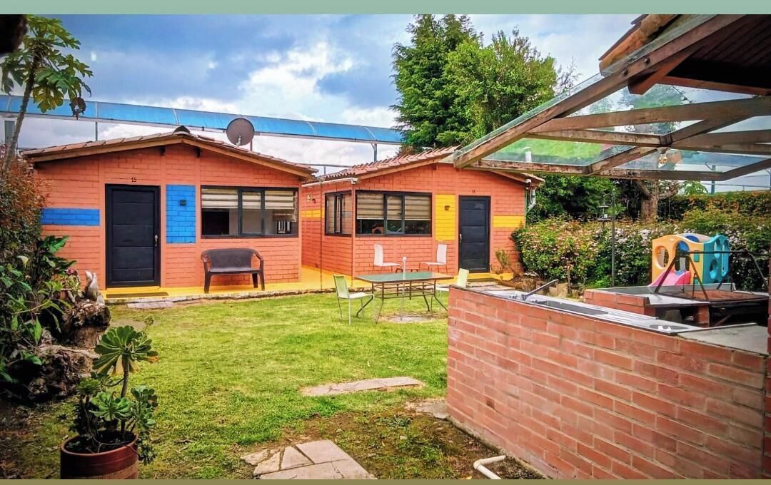 Un bâtiment à deux étages avec une façade en briques, un petit patio doté d’une table et de chaises, et un espace de jeux avec des équipements colorés.