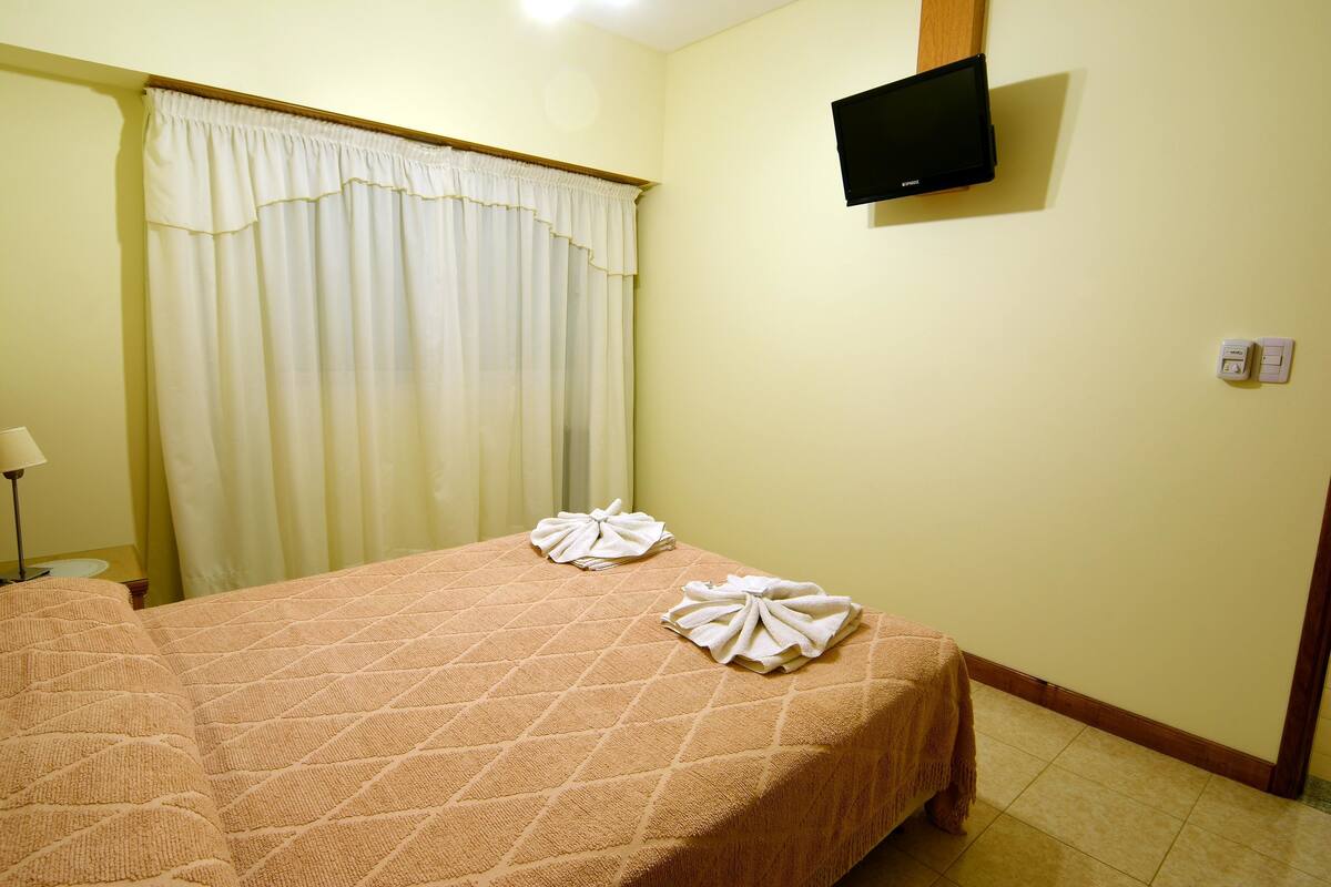 Une chambre d’hôtel avec un lit, un téléviseur fixé au mur et une fenêtre avec des rideaux.