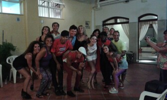 Un grupo de personas en una habitación con piso de baldosas, una ventana con rejas y una puerta con cortinas.