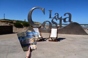 Suuri metallinen kyltti, jossa lukee ”La Costa”, ja sen edessä kaksi maalaustelineitä, joissa on tyhjät kankaat.
