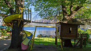 A playground with a slide, swings, and a small wooden structure near a lake. - Los Castaños (San Carlos de Bariloche)