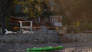 A lakeside cabin with a stone wall, a green kayak, and outdoor furniture. - Los Castaños (San Carlos de Bariloche)