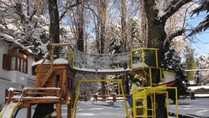 A playground with yellow equipment and a wooden climbing structure, surrounded by snow-covered trees. - Los Castaños (San Carlos de Bariloche)