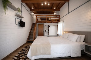Ein Schlafzimmer mit Bett, einer Holztreppe, einem an der Wand montierten Fernseher und einer Pflanze auf einem Regal.