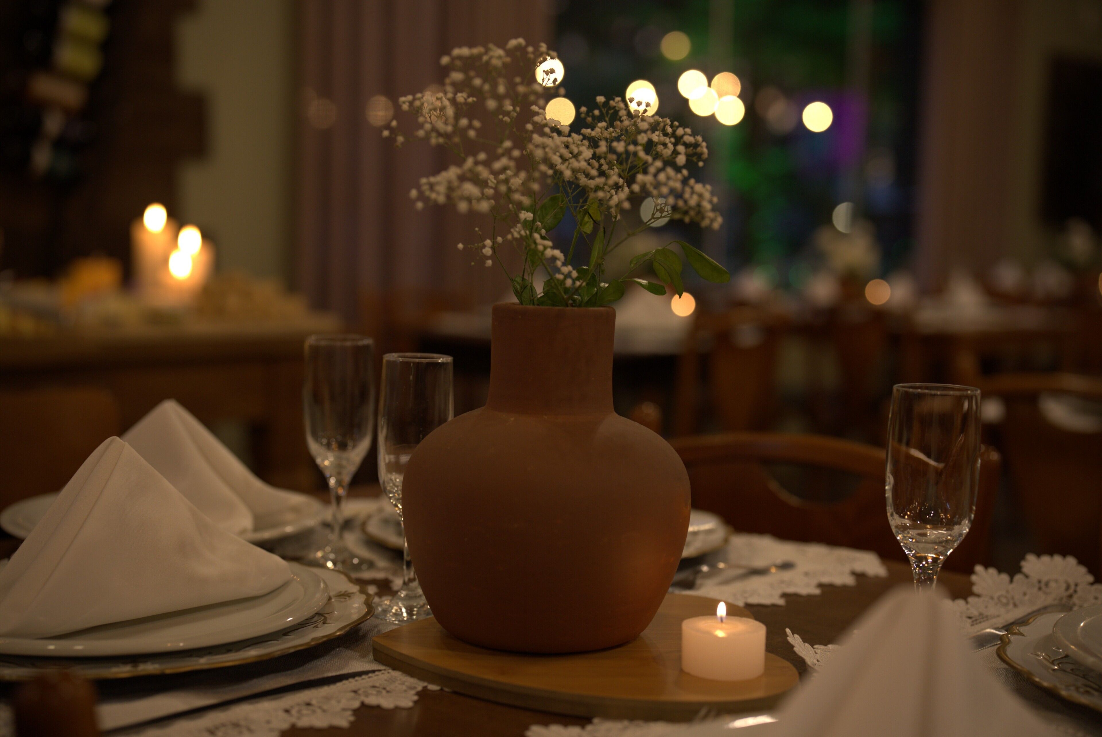 Una mesa de comedor lista con platos, un florero con flores, una vela y copas de vino.