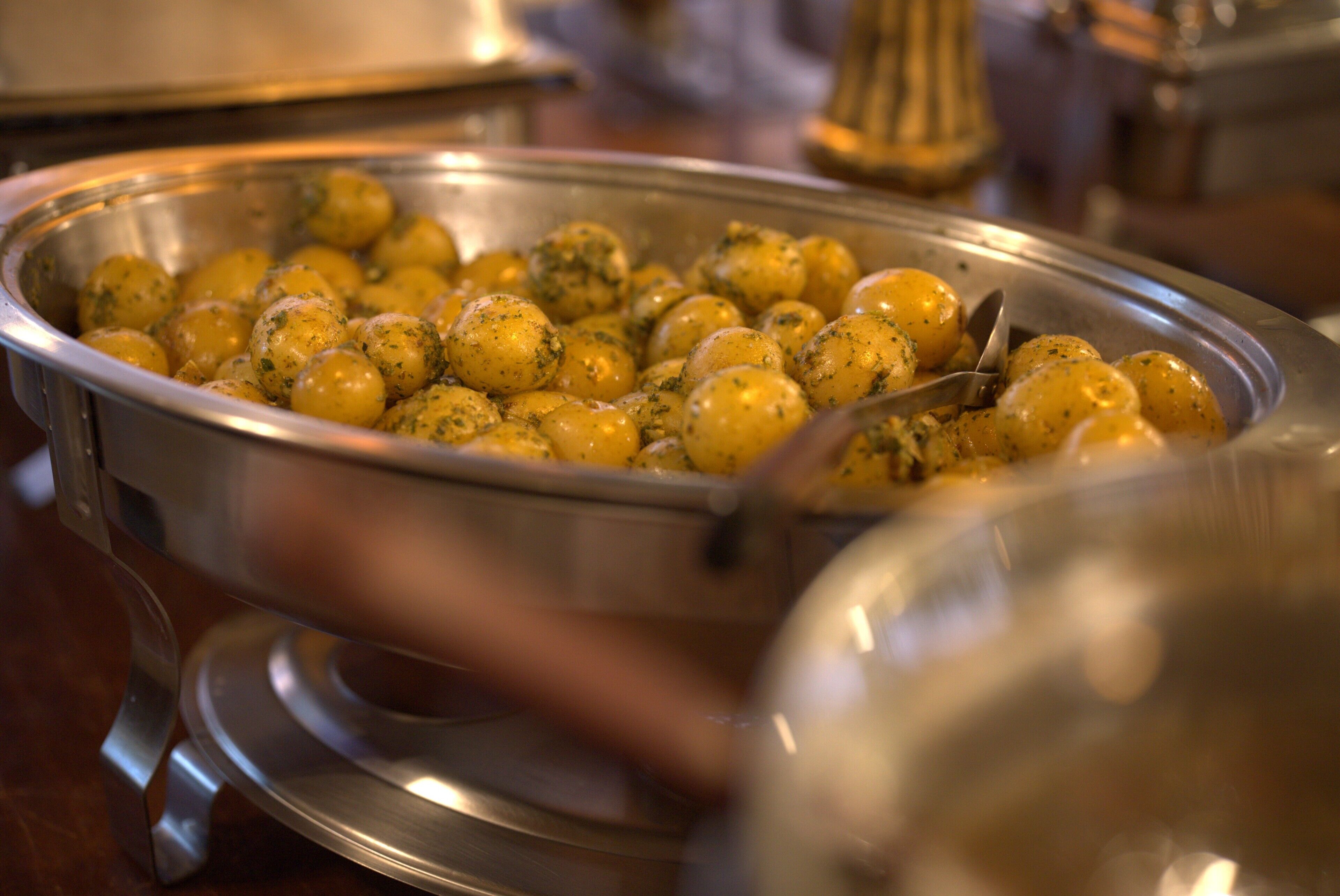 A metal serving dish with round, seasoned potatoes.