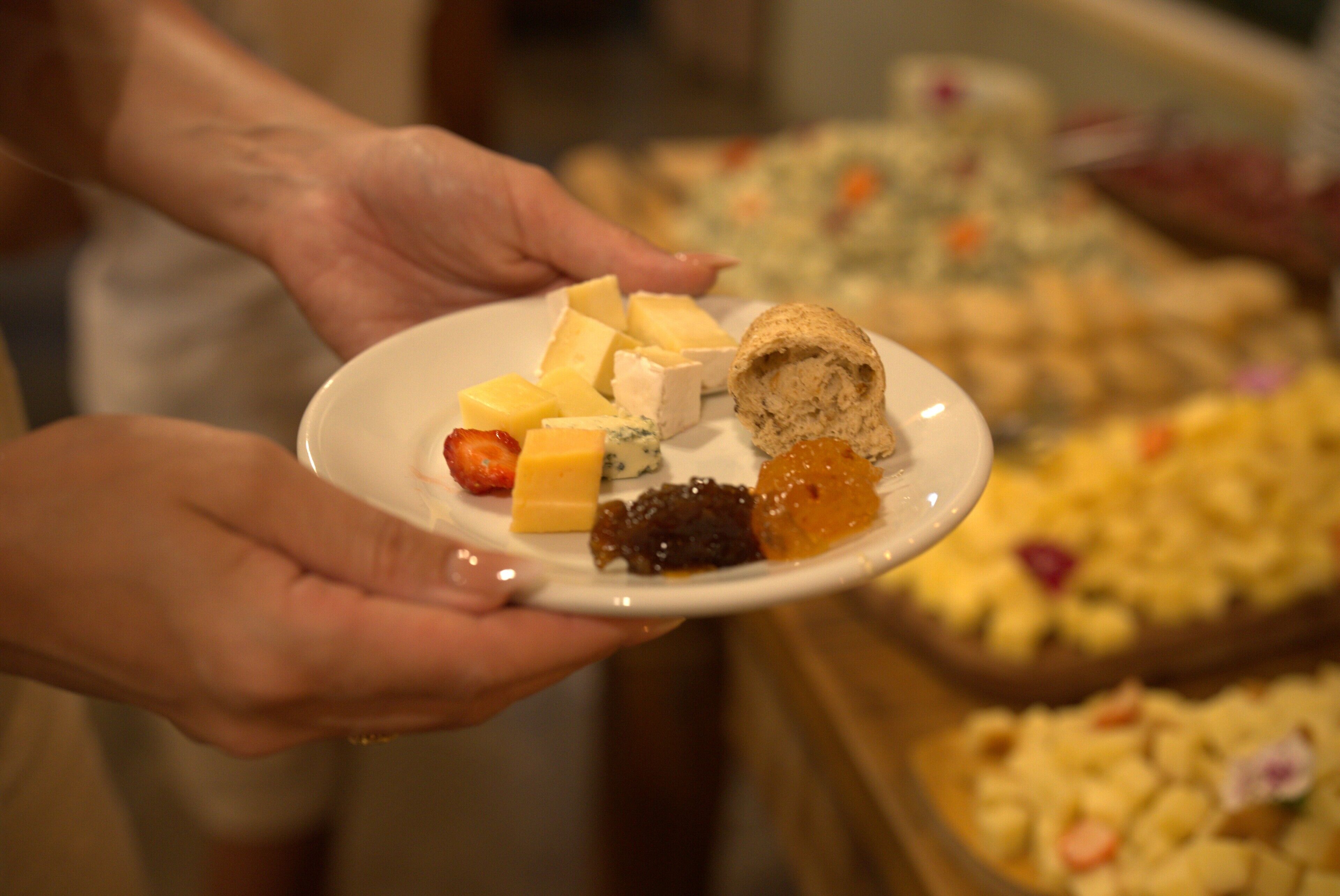 A person holding a plate with various cheeses and a bread roll.
