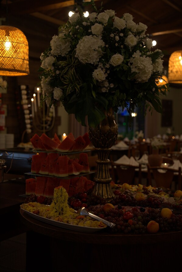 A dining table with a floral centerpiece, a variety of fruits, and a candle holder. - Hotel Acqua Lokos (Capao da Canoa)