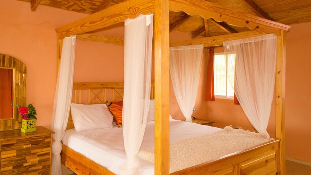 Een bed met hemelbed voorzien van witte lakens, een houten hoofdbord en een nachtkastje met een bloevas.