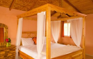 Een bed met hemelbed voorzien van witte lakens, een houten hoofdbord en een nachtkastje met een bloevas.