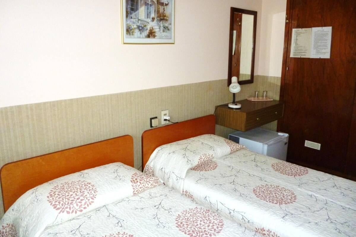 Ein Zimmer mit zwei Betten, einem Holzschrank, einem Spiegel und einem Bild an der Wand.