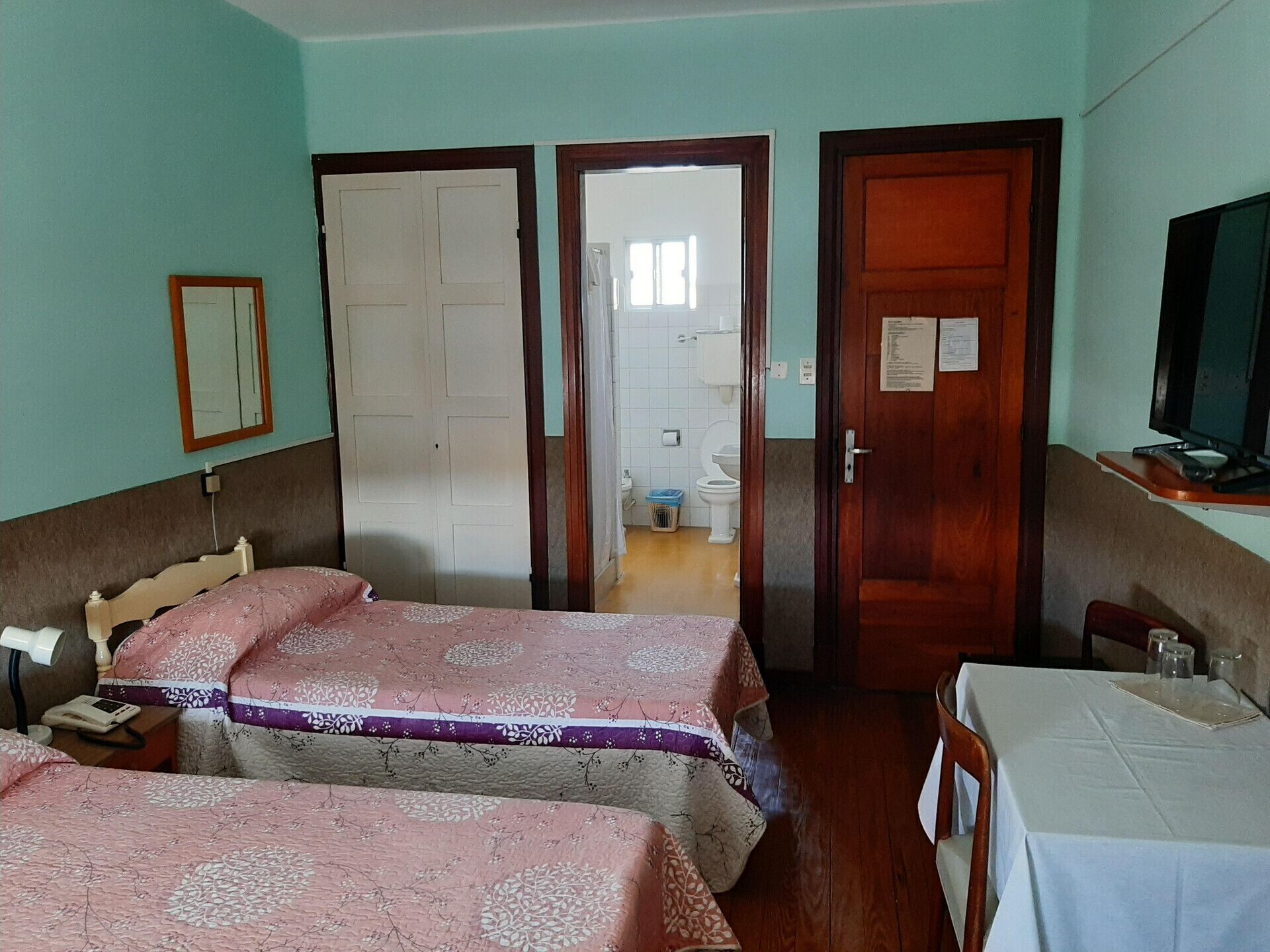 A hotel room with two beds, a desk, a chair, a television, and a bathroom visible through an open door.