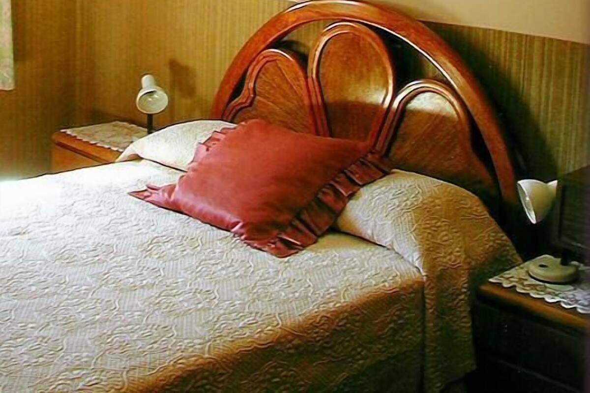 Ein ordentlich bezogenes Bett mit einem Holz-Kopfteil, einem roten Kissen und einem weißen Kissen.