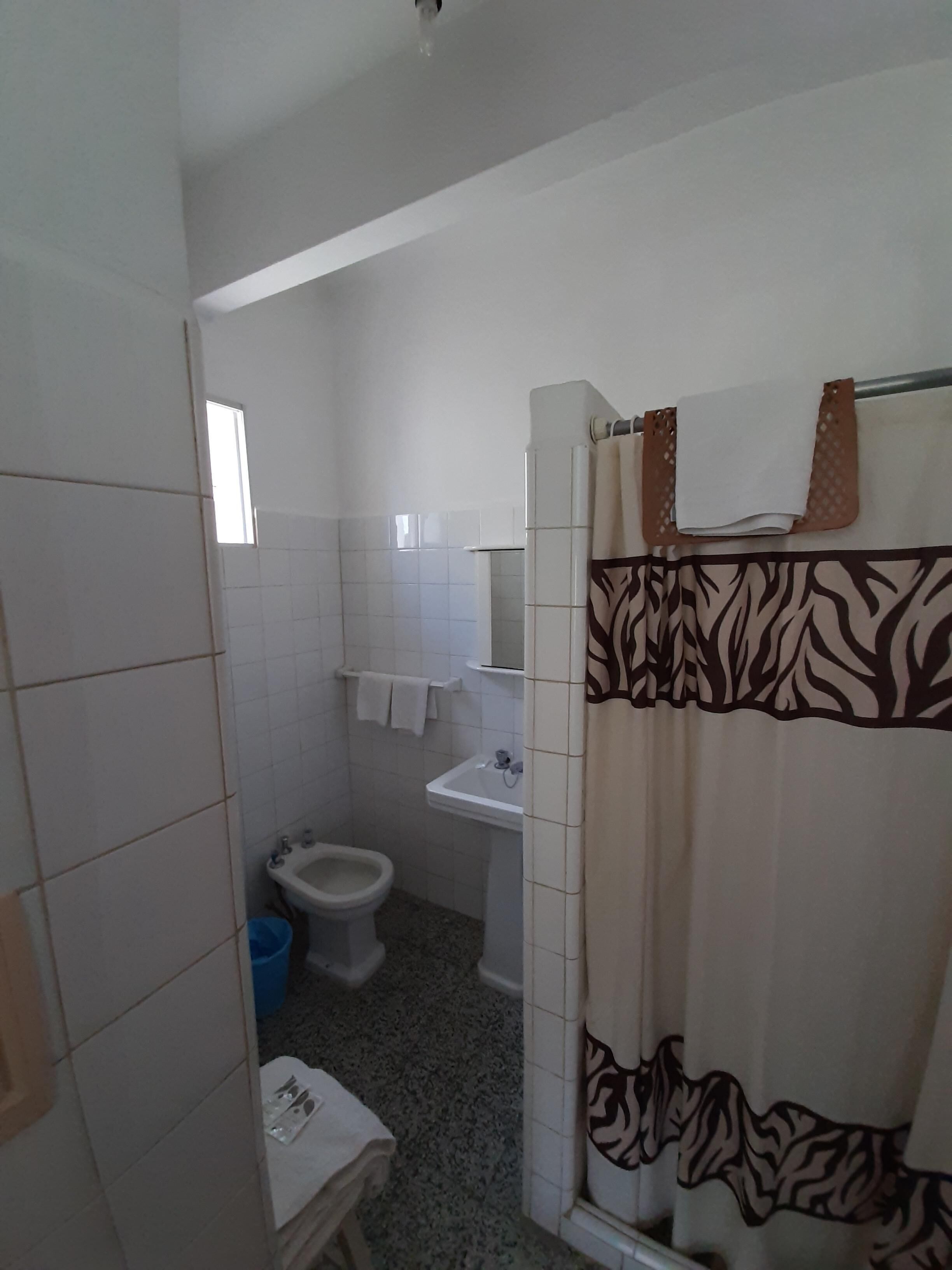 Un baño pequeño con azulejos blancos, un lavabo, un inodoro y una cortina de ducha con estampado de cebra.