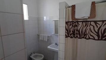 Un baño pequeño con azulejos blancos, un lavabo, un inodoro y una cortina de ducha con estampado de cebra.