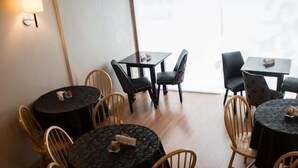 Un comedor con mesas y sillas redondas, algunas con manteles negros y otras con manteles oscuros estampados.