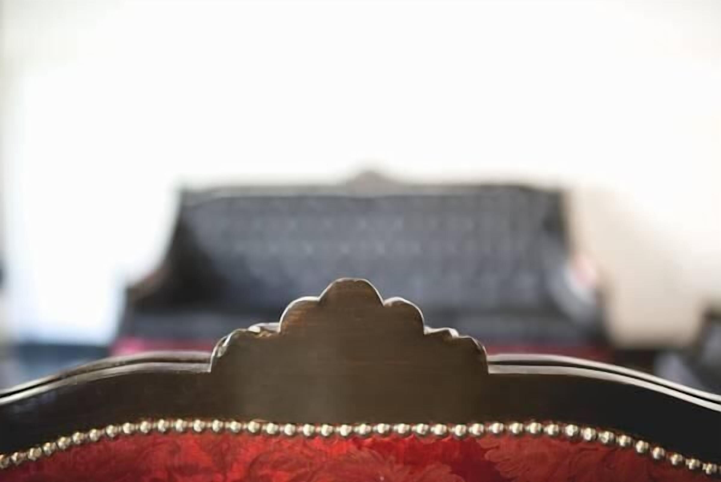 A close-up of a chair with a decorative backrest and a red upholstered seat.