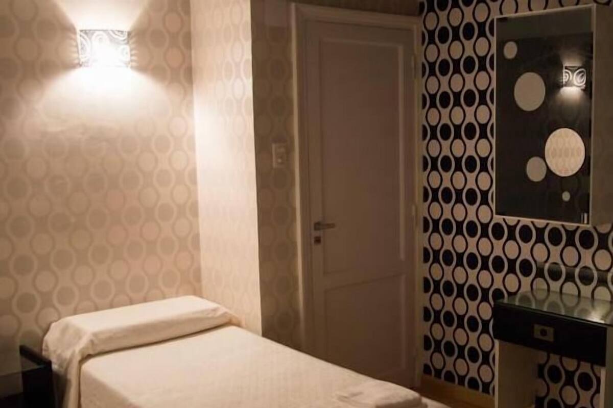 A hotel room with a bed, a bedside table, a mirror, and a patterned wall.