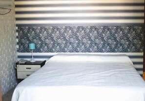 Une chambre d’hôtel avec un lit, une table de chevet, une lampe et un mur décoré d’un motif.