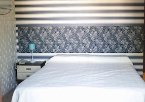 Una habitación de hotel con cama, mesita de noche, lámpara y un papel tapiz estampado.