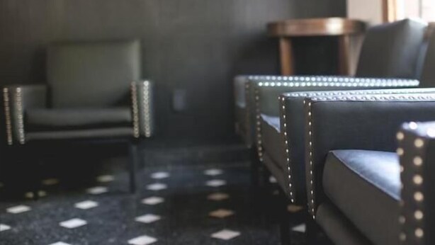 Una habitación con piso oscuro, un sillón verde y un sofá de cuero negro con detalles de tachuelas.