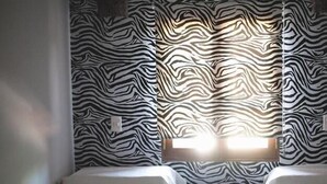 Habitación con dos camas, papel tapiz a rayas de cebra y un ventanal que deja entrar luz natural.