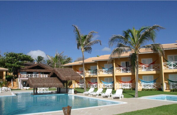 A hotel with a swimming pool, lounge chairs, and palm trees. - Bouganville Hotel (Beberibe)