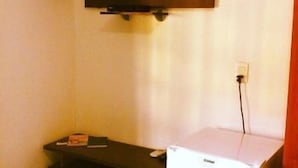 Una habitación con una televisión de pantalla plana montada en la pared, un refrigerador blanco y un escritorio de madera oscura con una silla.