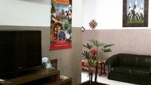 Una sala de estar con una televisión, un sofá de cuero negro, un mueble de madera y un cartel en la pared.