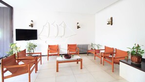 Una sala moderna con un televisor de pantalla plana, sillones naranjas, una mesa de centro de vidrio y arte decorativo en la pared.