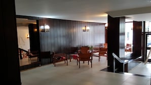 Un vestíbulo de diseño moderno, con una zona de estar que incluye sillas de madera y una mesa, una escalera y una pared con paneles de madera verticales.
