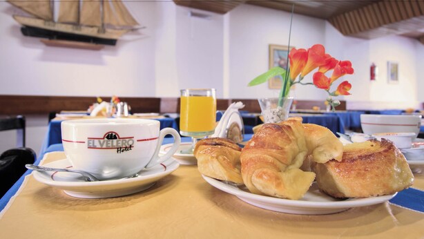 Una mesa de desayuno con una taza que dice "ELVELO HOTEL", un vaso de jugo de naranja y croissants.