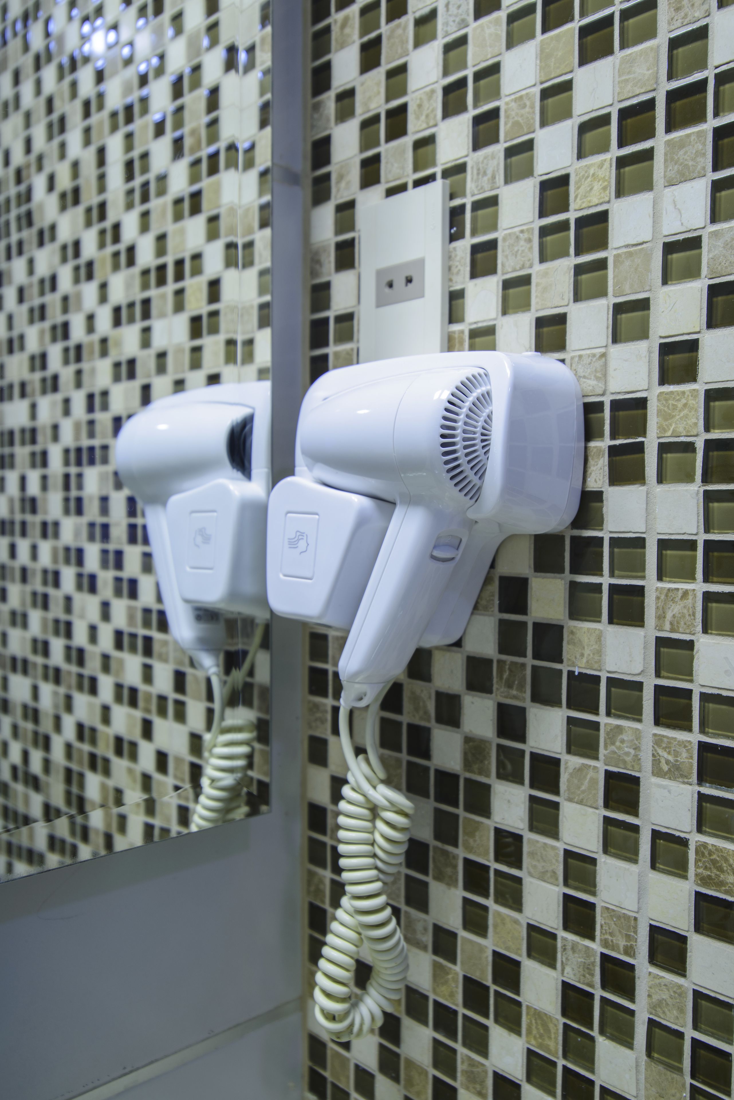 Un secador de pelo fijado a una pared de azulejos con un enchufe.