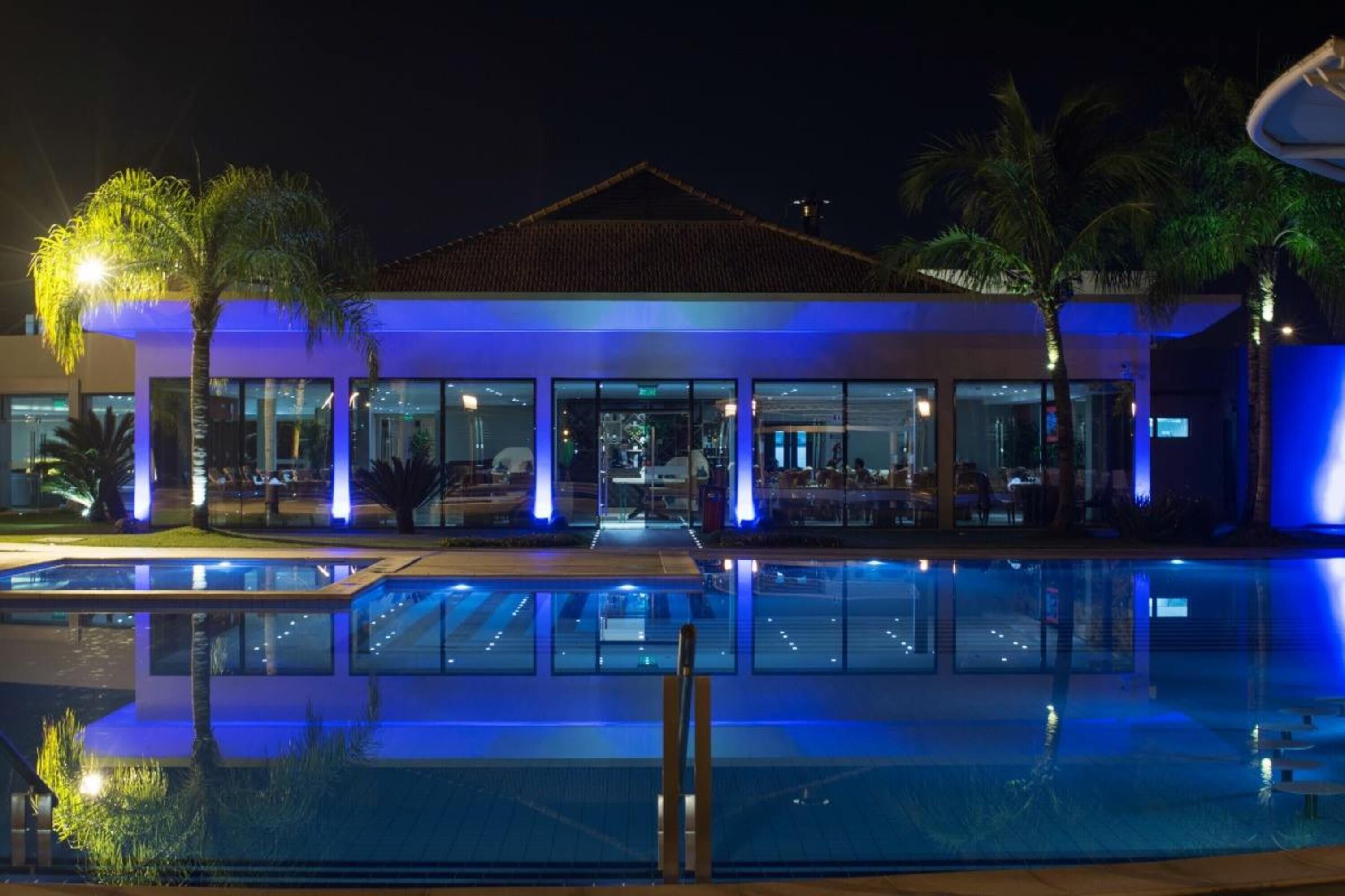 A modern hotel with a pool area, large windows, and palm trees.