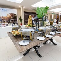 A buffet setup with various food stations and a large decorative plant.