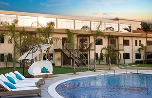 A modern building with a swimming pool, lounge chairs, and palm trees.