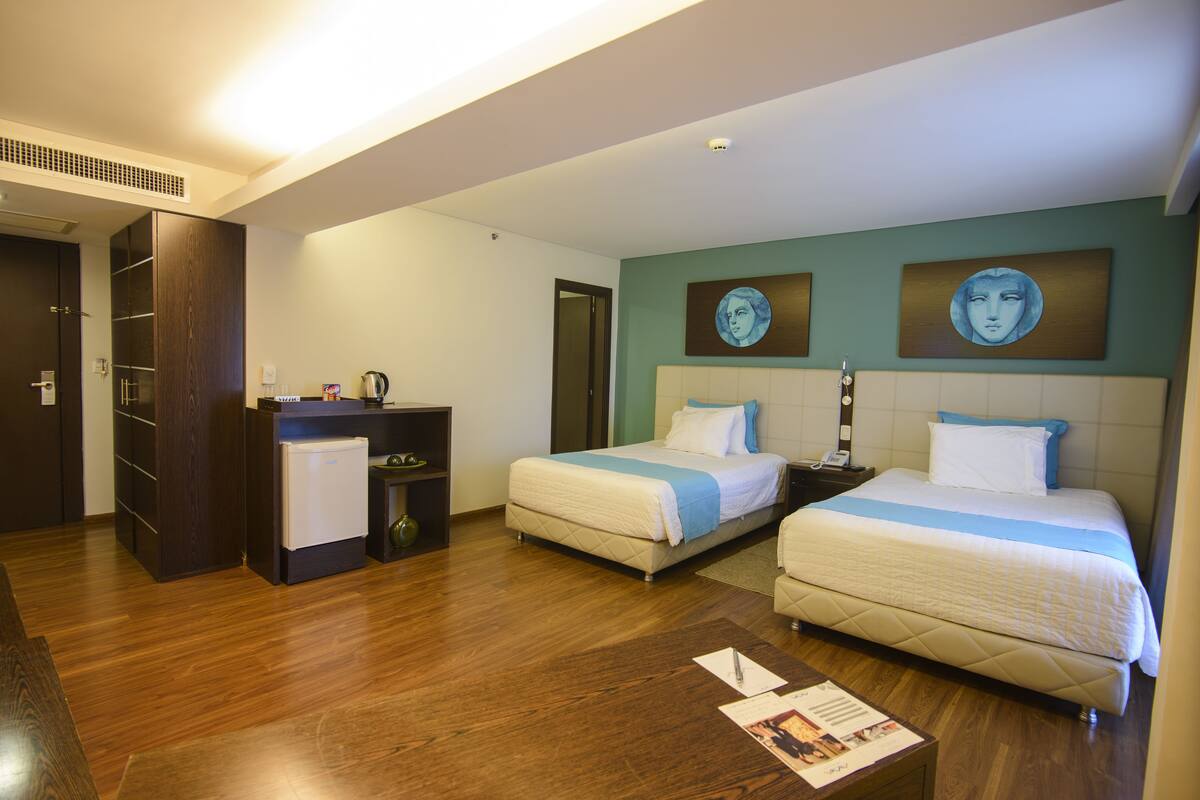 A hotel room with two beds, a desk, a wardrobe, and a small kitchenette.