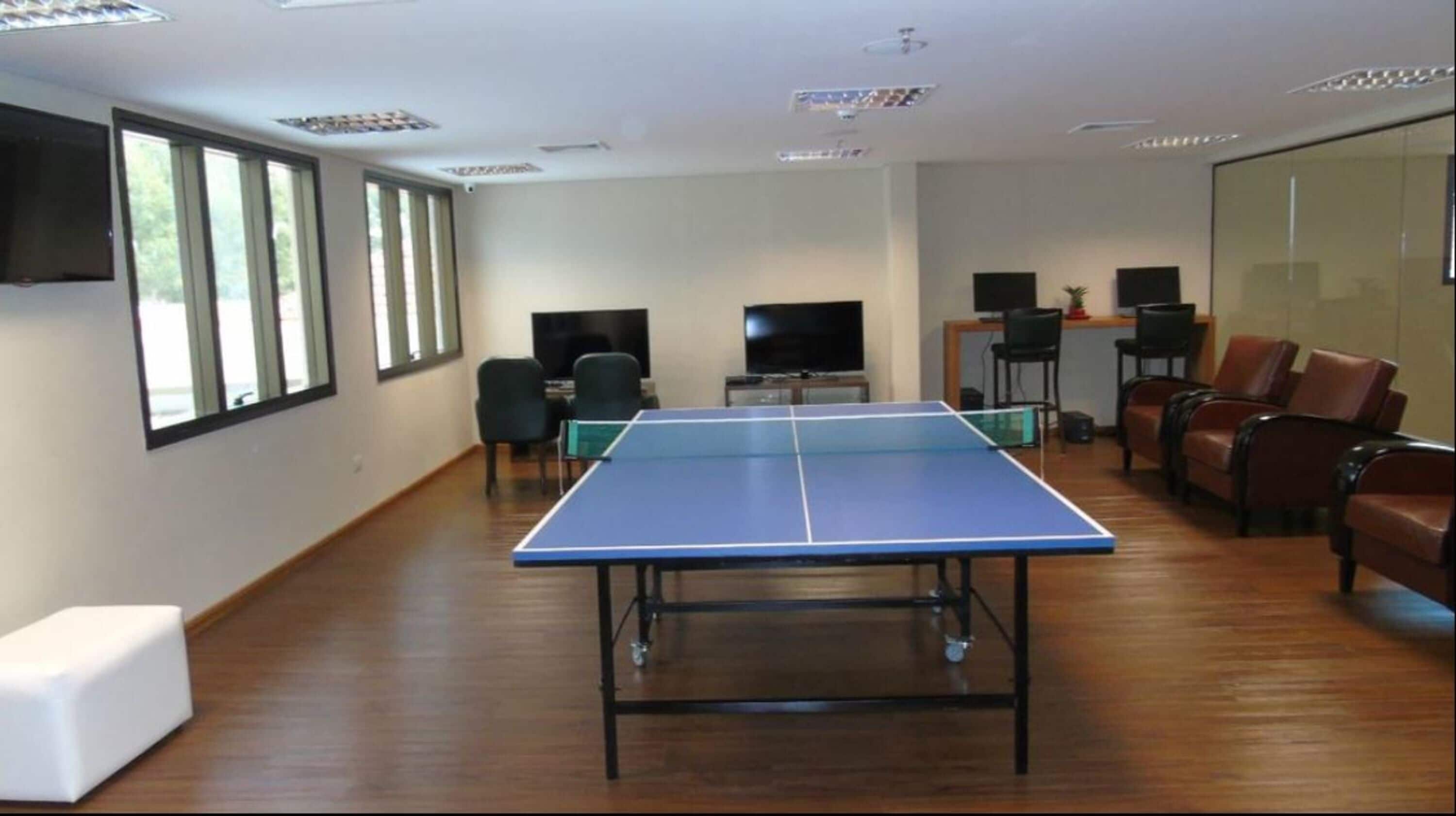 A room with a ping pong table, chairs, a TV, and a large window.