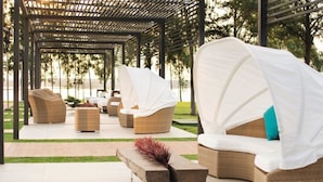 Un espacio de estar al aire libre cubierto con mobiliario de mimbre y toldos blancos.