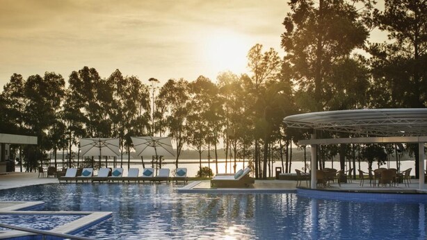 Una piscina con sillones y sombrillas, rodeada de árboles y vistas al atardecer.