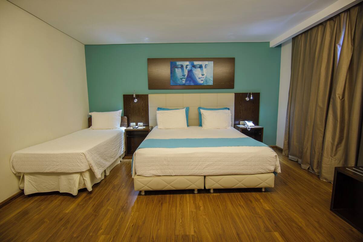 A hotel room with two single beds, a large bed, a painting on the wall, and a wooden floor.