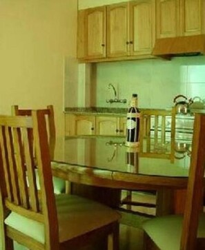 Une cuisine avec des meubles de rangement en bois, une table en verre et une bouteille de vin.